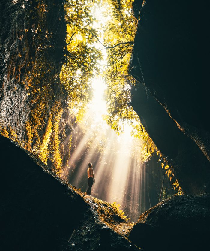 Adventurous person exploring a sunlit cave with vibrant foliage in Bali, Indonesia.